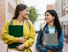 two women holding notebooks and smiling outside